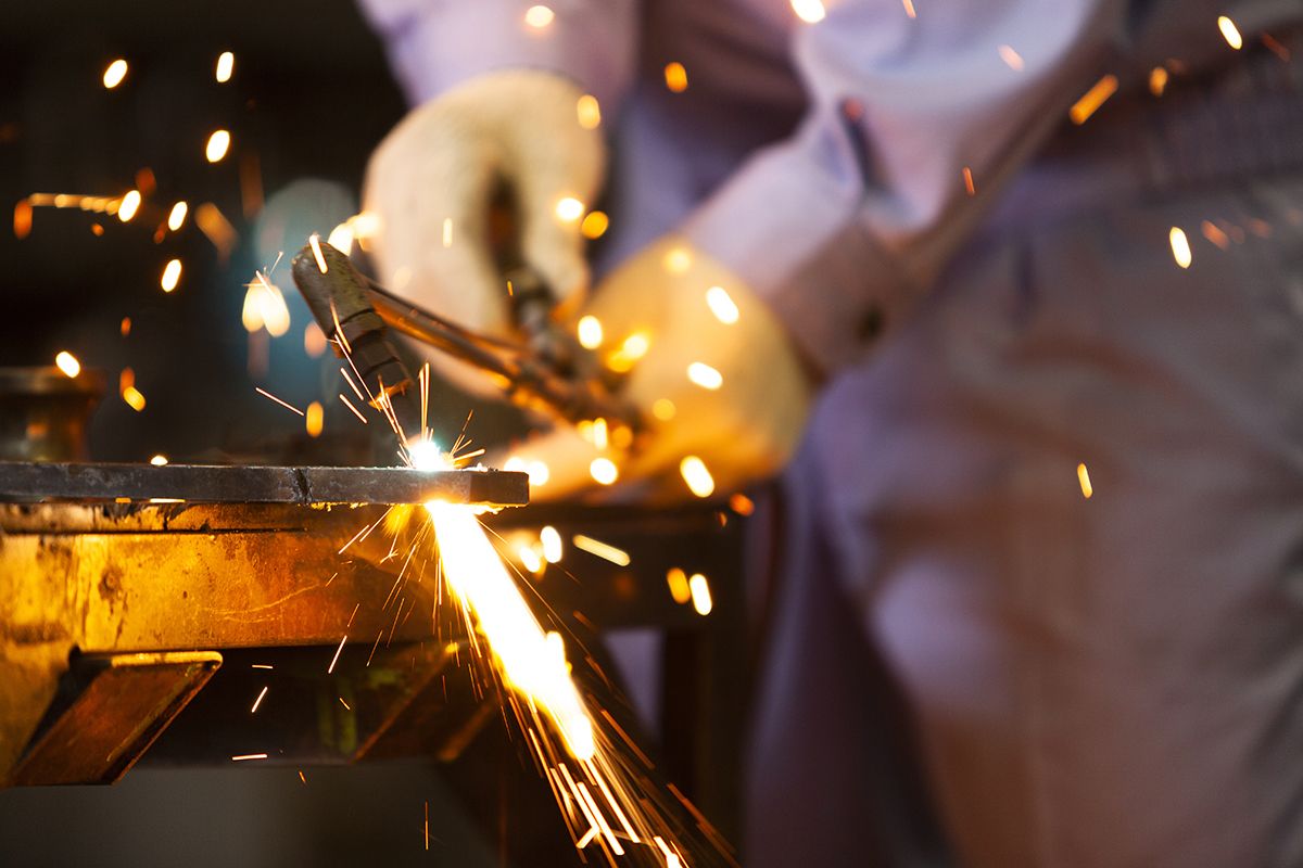 Person in Schutzkleidung arbeitet mit einer Lichtbogenschweißmaschine und erzeugt einen Funkenflug.