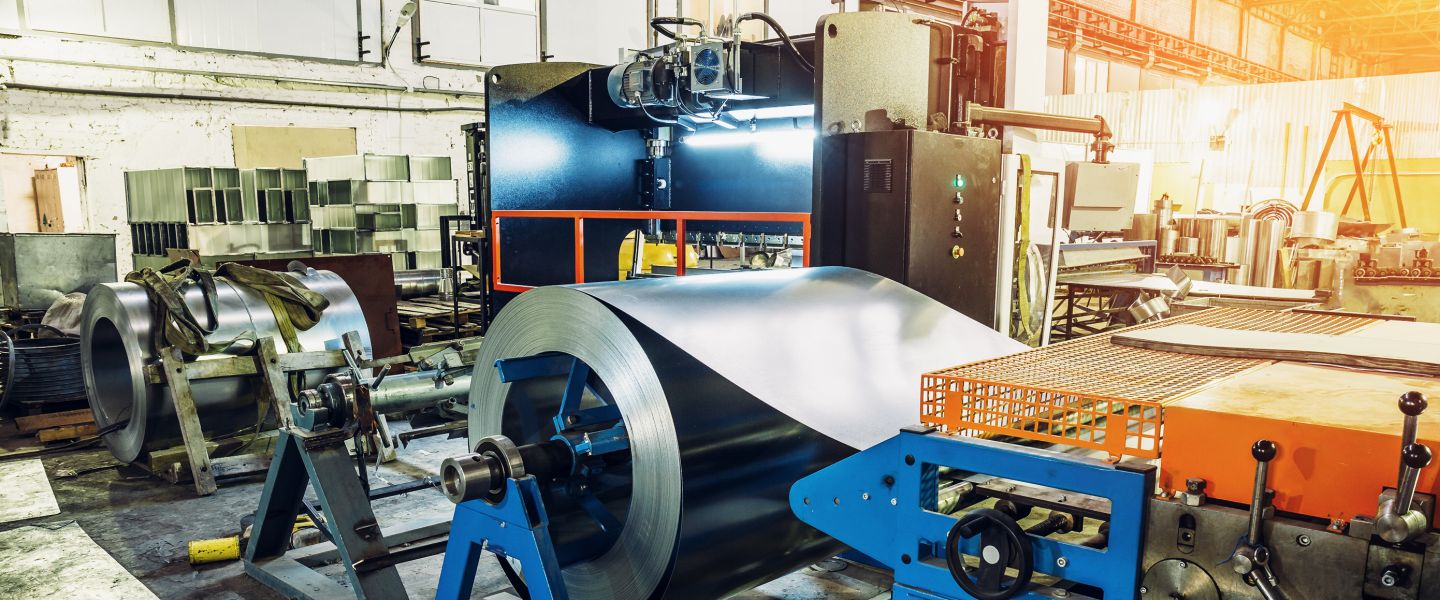 Metallverarbeitung in einer Werkshalle, in der verschiedene Maschinen und Walzen stehen.