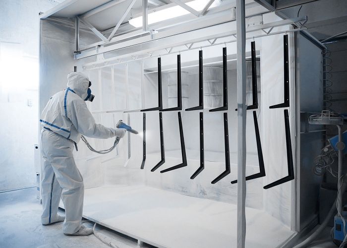 Person in weißer Schutzkleidung bringt weißen Pulverlack mit Pulverpistole in der Pulverkabine auf.