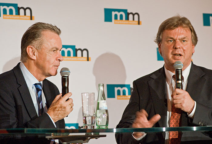 Fußballtrainer Ottmar Hitzfeld und m+m Geschäftsführer Michael Müller in einem Podiumsgespräch vor einer m+m Logowand.