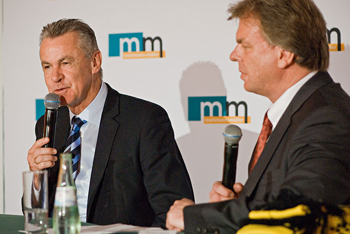 Fußballtrainer Ottmar Hitzfeld und m+m Geschäftsführer Michael Müller in einem Podiumsgespräch vor einer m+m Logowand.