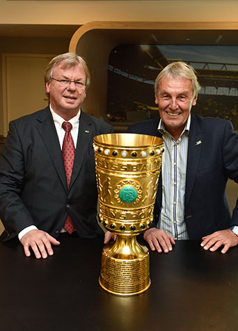 Fernsehmoderator und Sportreporter Jörg Wontorra und m+m Geschäftsführer Michael Müller stehen hinter dem DFB-Pokal. 